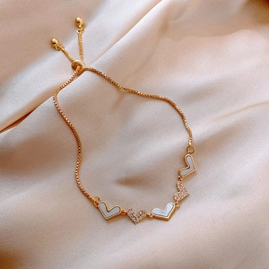 Elegant gold heart bracelet with white shell inlay and zircons on silk background