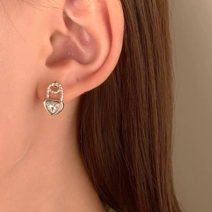 Nahaufnahme von herzförmigem Silberohrring mit Zirkonia und Schloss-Design am Ohr