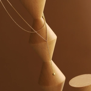 Detailed view of gold Y-shaped fringe necklace draped over minimalist wooden props