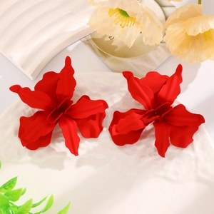 Macro shot of oversized matte red flower earrings on a textured white porcelain plate