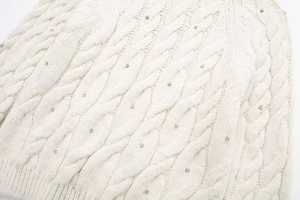 Detailansicht eines weißen Zopfstrickpullovers mit kleinen silbernen Strassverzierungen