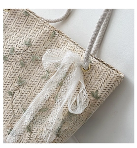 Detail of straw woven tote with romantic lace bow and green leaf embroidery