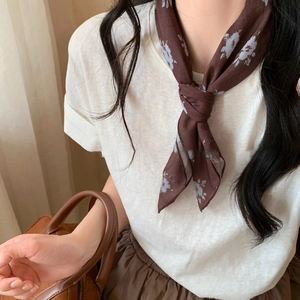 Close-up of floral pattern silk scarf in brown and light blue tied around a neck