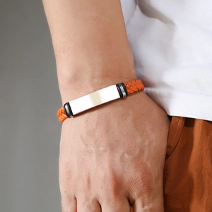 Detail of an orange braided leather bracelet with a polished silver metal plate on a male wrist