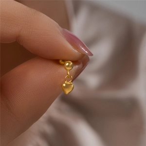 Macro shot of matte golden heart-shaped pendant earring held between fingers for size