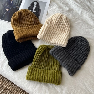 Chunky knit beanies in five versatile colors displayed on a textured white fabric background