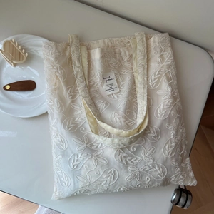 Detail of floral lace embroidery and woven label on a beige cotton canvas tote bag