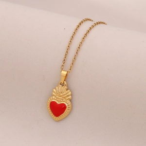 Close-up of golden necklace with red enamel heart pendant and crown design on soft fabric