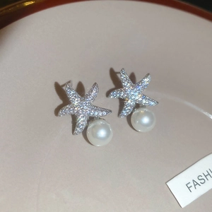 Gros plan sur des boucles d'oreilles étoile de mer avec pavé de zircons et perle ronde