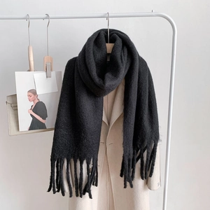 Detail of black thick knitted cashmere scarf with long tassels on a beige coat hanger