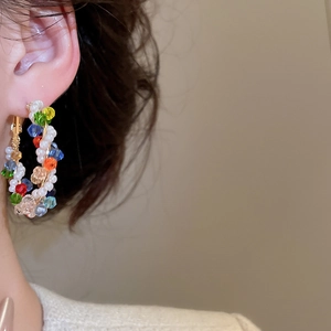 Close-up of colorful crystal beads and pearls on large gold hoop earrings worn by model