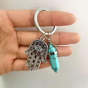 Hamsa hand keychain with turquoise hexagonal crystal pillar pendant held in hand