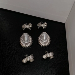 Three pairs of silver stainless steel bow earrings with pearls on black leather background