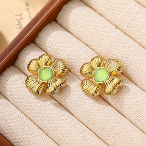 Elegant gold flower earrings with green emerald gemstone center on a jewelry box