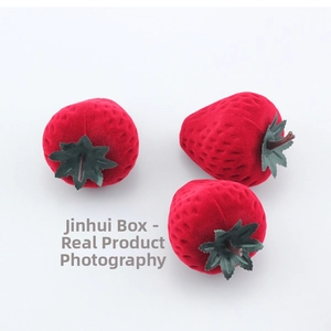 Detailed view of three red flocked strawberry-shaped jewelry boxes with green leaf accents