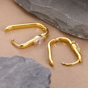 Detailed macro view of gold U-shaped earrings with marquise-cut zircon on textured fabric