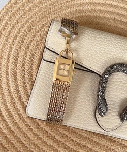 Close-up of gold square ladies watch with metal chain strap on beige leather bag