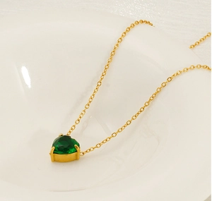 Close-up of a heart-shaped emerald pendant on a gold chain inside a ceramic dish