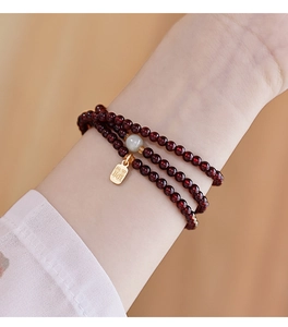 Close-up of red garnet beads bracelet with green jade and gold Fu charm on wrist