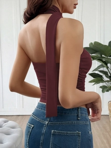 Detail of burgundy halter neck backless top in stretch fabric worn with blue jeans