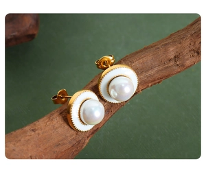 Macro shot of gold pearl disk earrings with white enamel on a natural dry branch