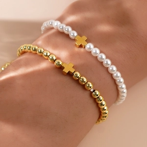 Close-up of stacked pearl and gold bead bracelets featuring minimalist cross charms
