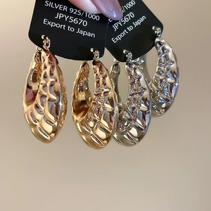 Close-up of chunky twisted hoop earrings in gold and silver finish with S925 engraving
