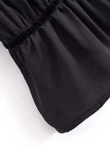 Detailed close-up of pleated black fabric texture and velvet ribbon stitching on blouse