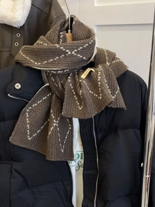 Detailed view of a brown plaid knitted scarf with a handmade label on a black puffer jacket