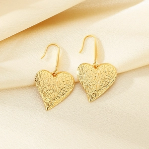 Golden heart earrings with textured surface on beige silk background, minimalist jewelry