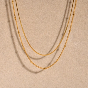 Close-up of golden double-layer necklace featuring a sleek snake chain and bead accents
