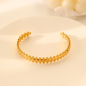 Detail view of gold stainless steel bangle with serrated edges on a ceramic tray