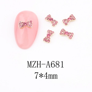 Detail view of 7x4mm gold bow nail charm with pink rhinestones on manicure