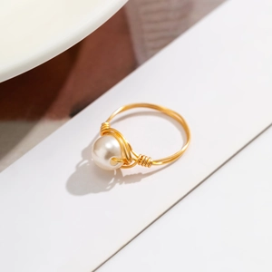 Macro view of handmade wire-wrapped golden ring featuring a lustrous white pearl detail