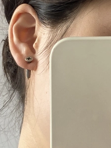 Detailed close-up of a punk-style stainless steel screw earring worn on an earlobe