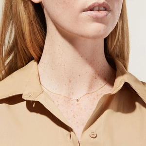 Close-up of a minimalist gold titanium necklace featuring a single zircon pendant on a model