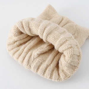 Macro detail of beige knit baby hat showing thick cable stitch texture and warm wool lining