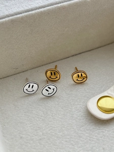 Détail de boucles d'oreilles smiley en argent et or sur un plateau en velours gris