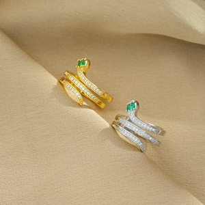 Detail shot of gold and silver snake rings with sparkling green emerald eyes on beige fabric