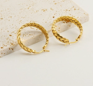 Detailed macro of 18K gold plated wheat pattern hoop earrings on a stone platform