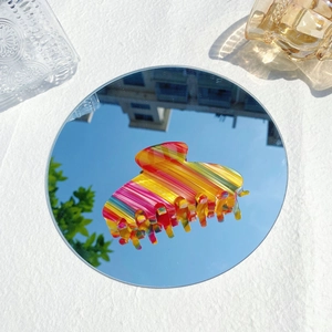 Pince à cheveux colorée en acétate avec rayures arc-en-ciel sur une surface miroir