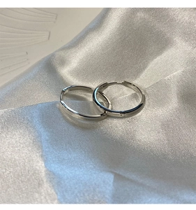 Dettaglio di orecchini a cerchio in argento minimalisti su tessuto di seta bianca