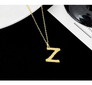 Macro detail of gold letter Z pendant with lava texture and zircon stones on a fine chain