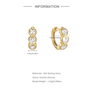 Macro detail of 925 silver golden huggie earrings with triple heart-shaped cubic zirconia