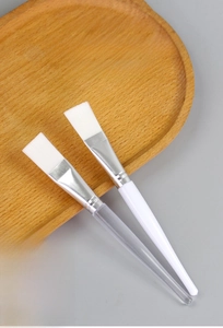 Detail of clear and white solid handles on cosmetic face mask brushes with silver ferrules