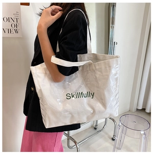 Detail of transparent PVC tote bag with white canvas interior and green lettering
