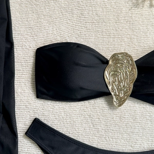 Detail of black bandeau bikini top featuring a gold sculptural oyster-shaped metal buckle