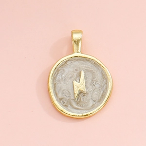 Detail of round gold-plated pendant featuring textured beige inlay and a lightning bolt charm