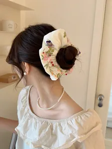 Close-up of a white satin scrunchie with floral embroidery worn by a model