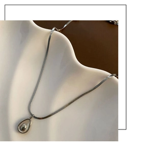 Detailed view of a silver teardrop pendant on a flat snake chain against a ceramic tray